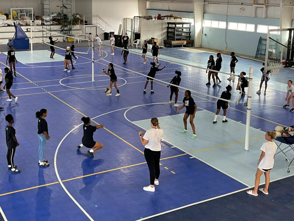 Indoor gymnasium filled with students practicing volleyball skills.