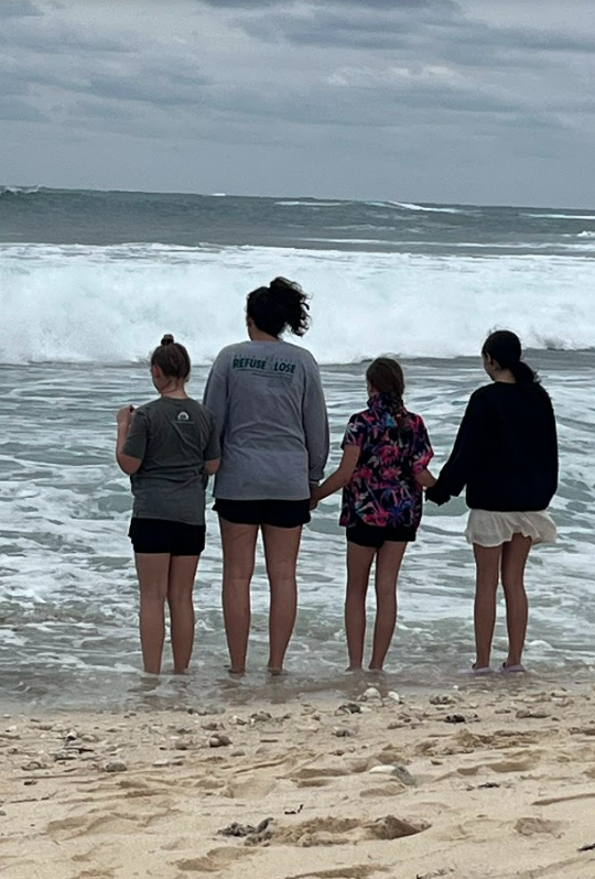 Four team members holding hands, standing in the waves on the beach