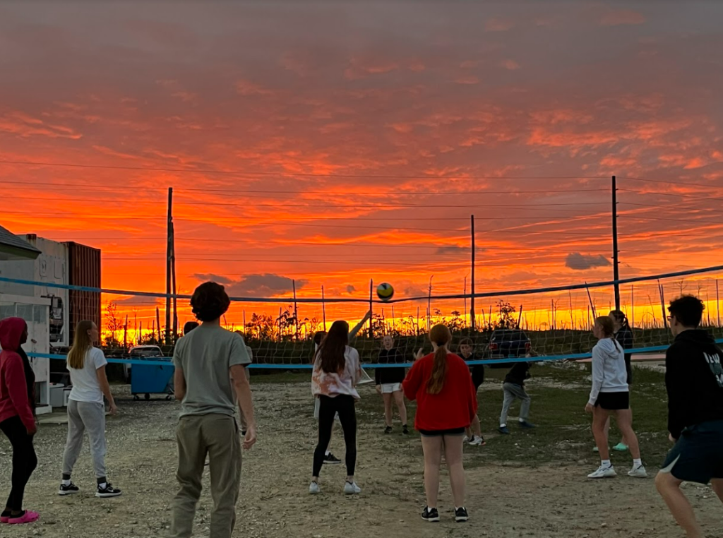 Students at Youth night playing volleyball with a beautiful orange and yellow sunset background.