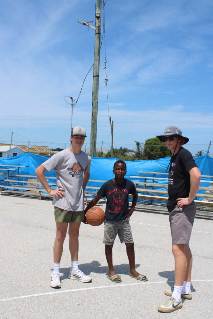 Two team members pose on the basketball court with their new friend who came to play in the pick up game.