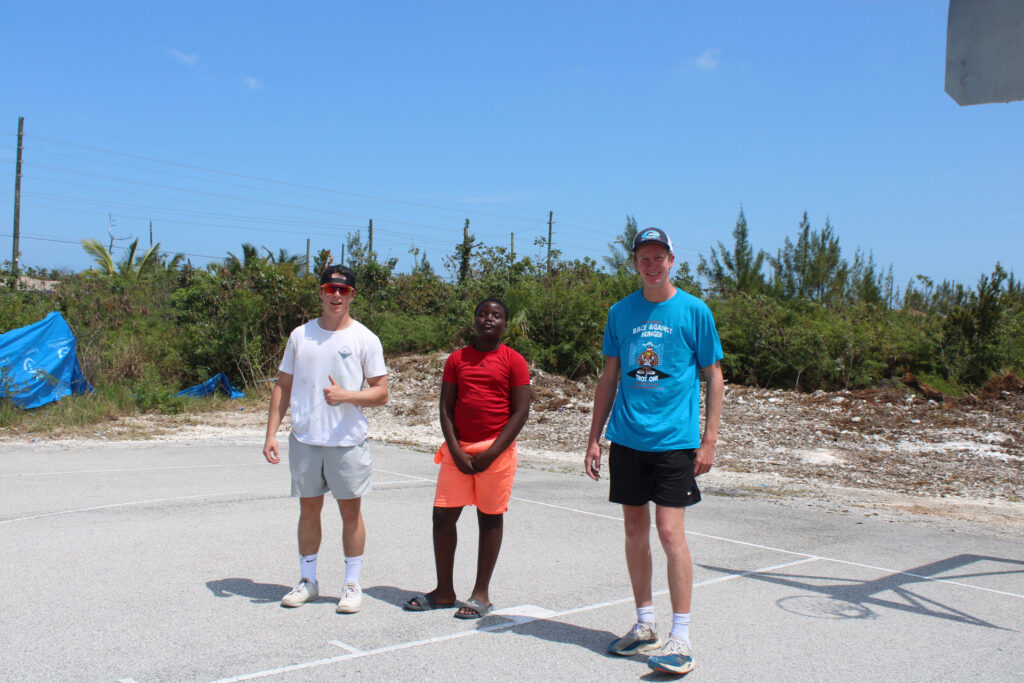 Two team members stand with another community member ready for a pick up game